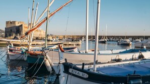 A marina with several boats docked, a stone building in the background, and calm water.