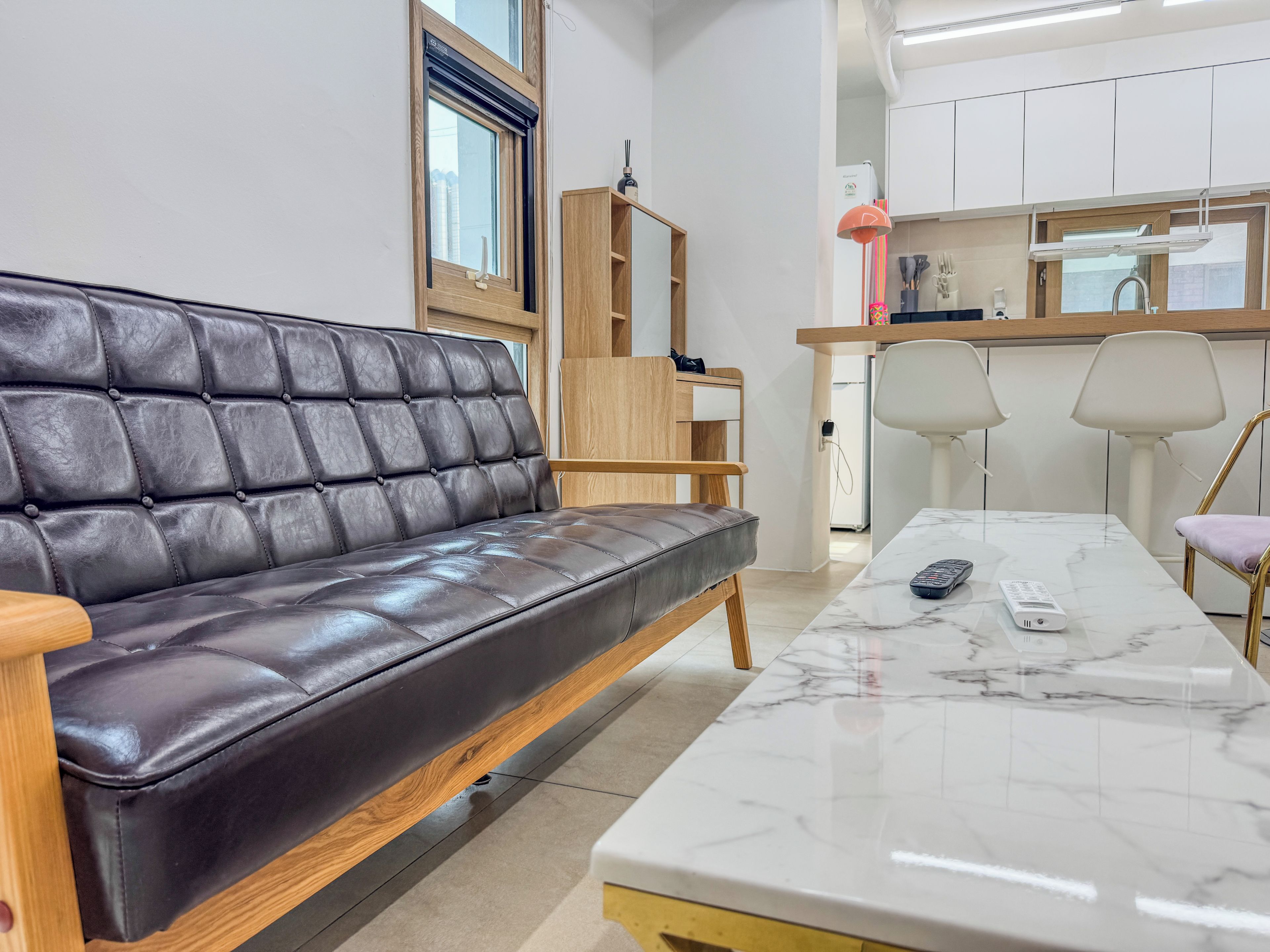 A modern living room with a leather sofa, a marble coffee table, and a kitchen area with white cabinets and a wooden countertop.