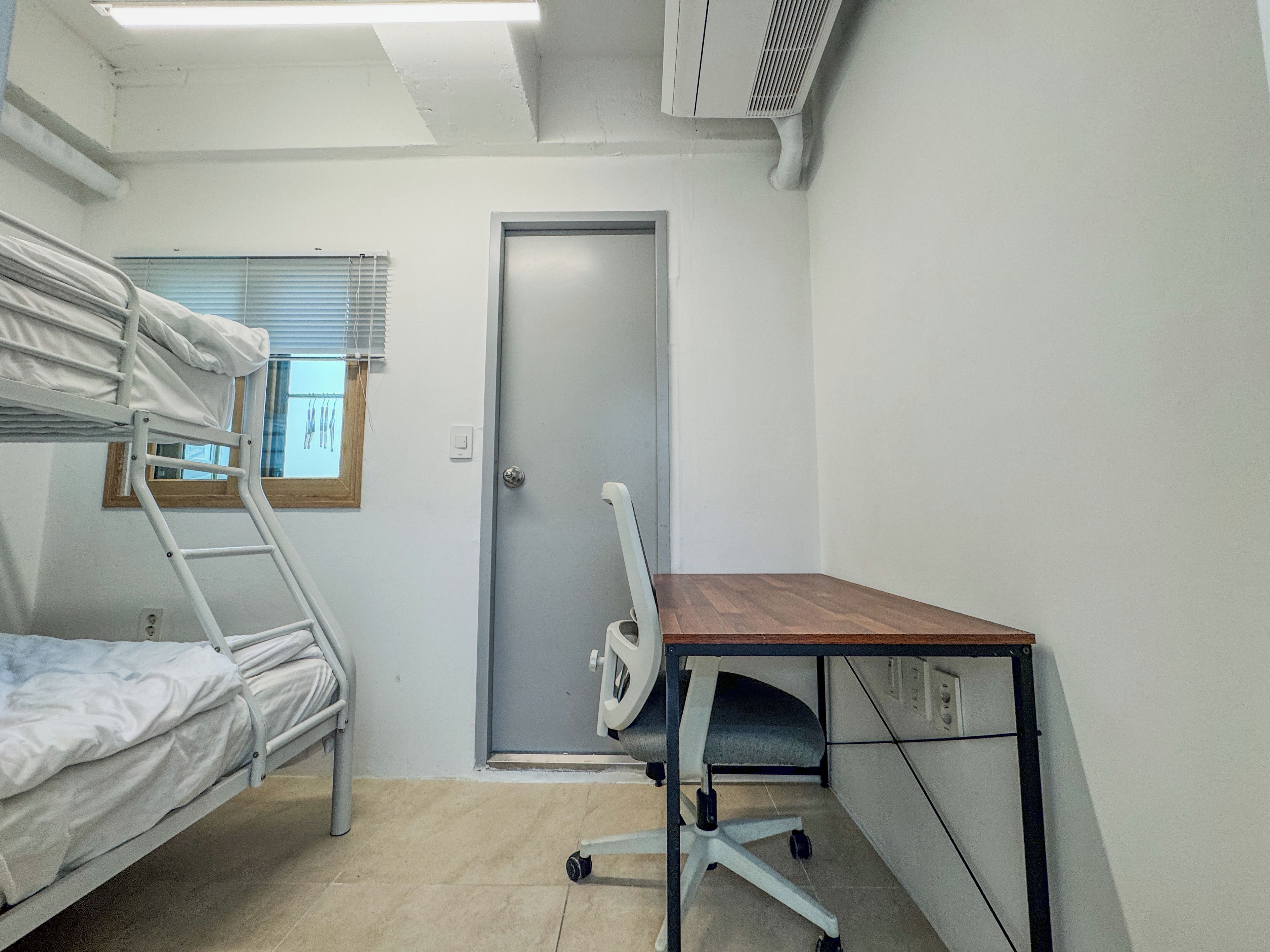 A bunk bed with a window, a desk with a chair, and a door.