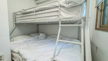 A bunk bed with white bedding, a window with blinds, and a white wall.
