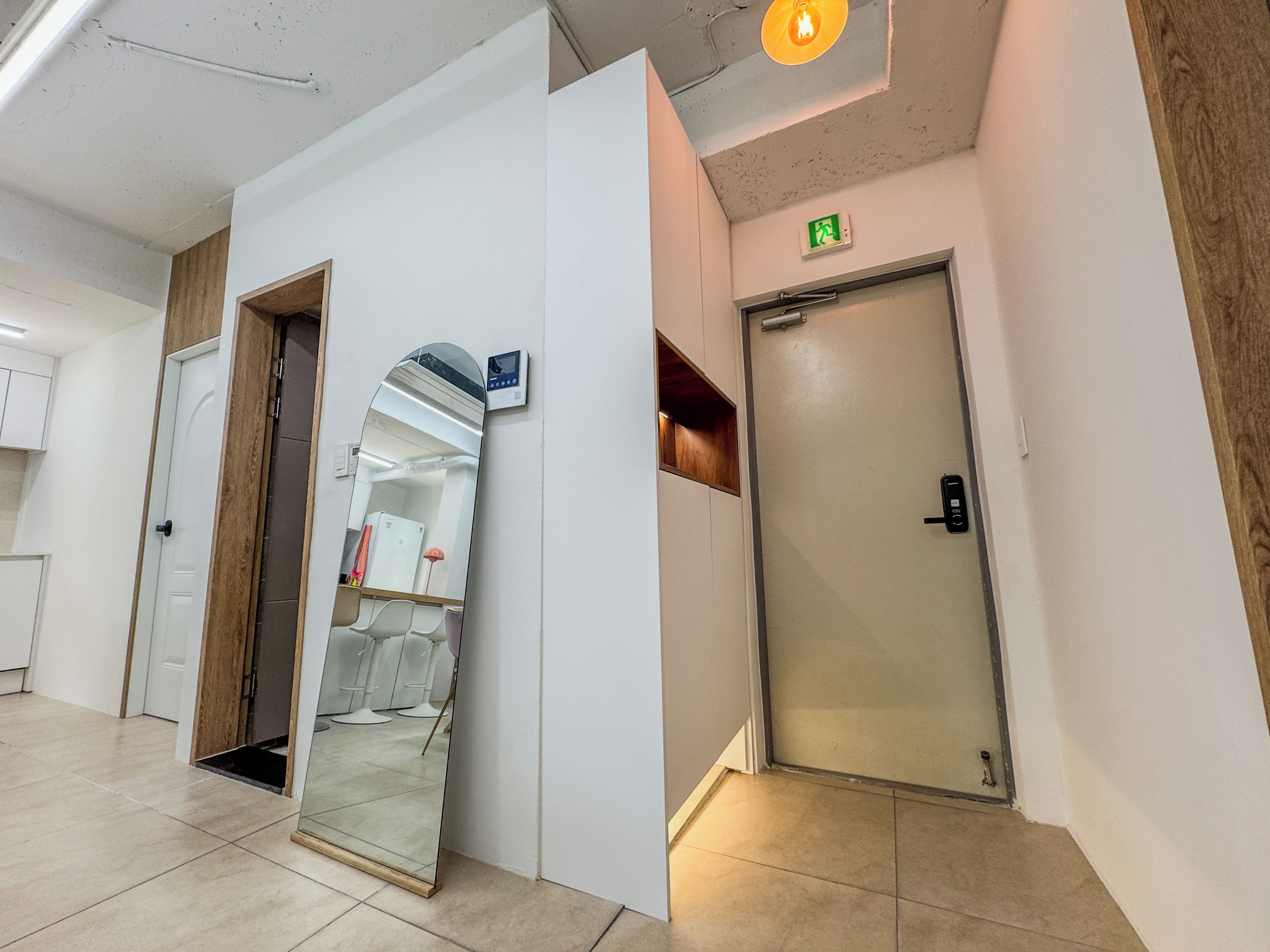 A hallway with a mirrored wall, a door with an emergency exit sign, and a ceiling light fixture.