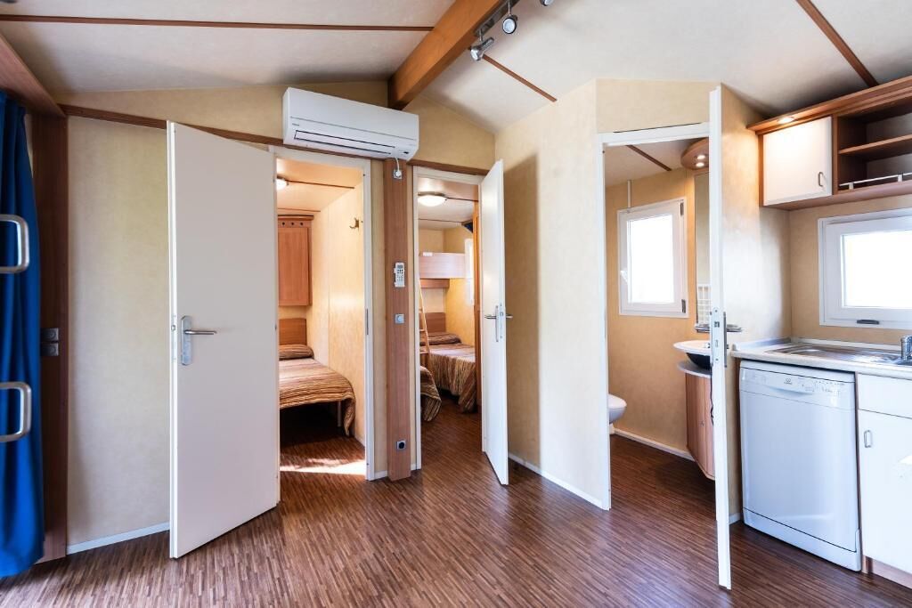 A compact RV interior with a kitchenette, a bed, and a bathroom.