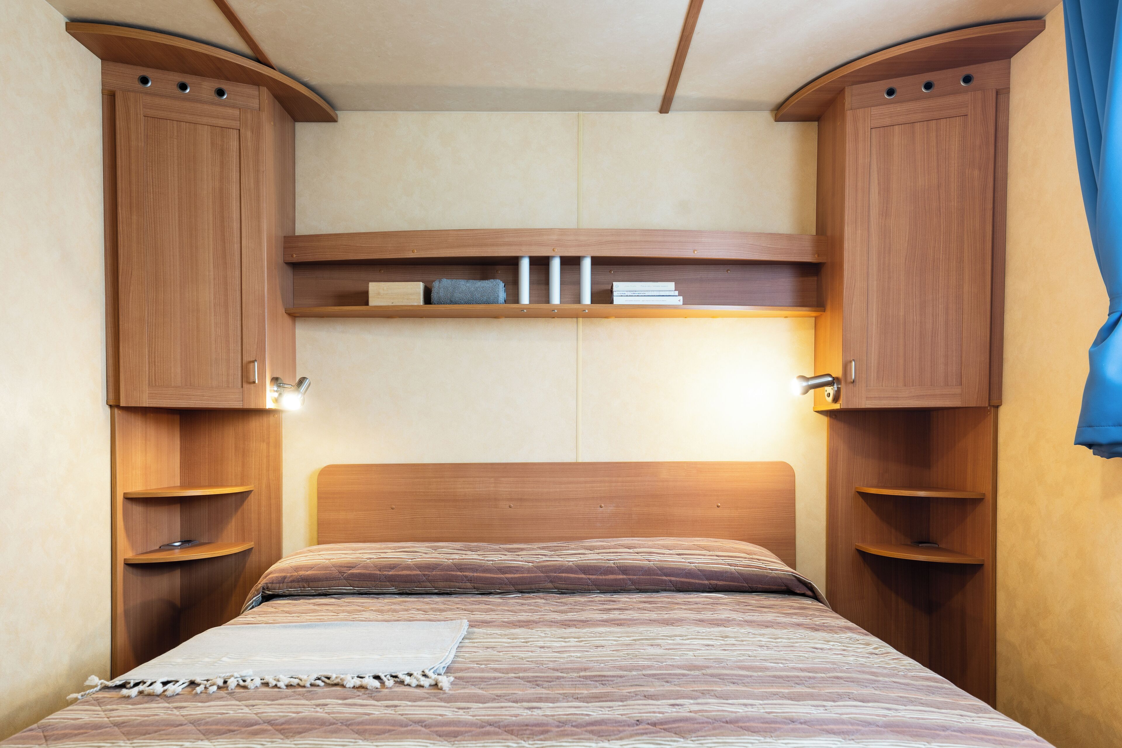 Un dormitorio con cabecera de madera, estanterías empotradas y una cama con colcha estampada.