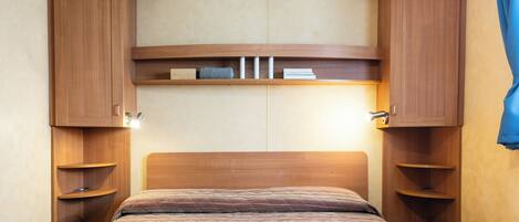 Un dormitorio con cabecera de madera, estanterías empotradas y una cama con colcha estampada.