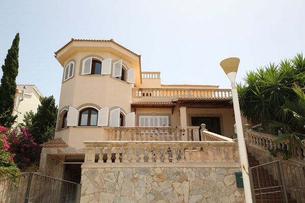 A two-story building with a stone facade, a balcony with balustrades, and a staircase leading to the entrance. - YourIsland Villa Son Serra (Son Serra de Marina)