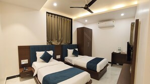 Ein Hotelzimmer mit zwei Betten, einem Deckenventilator, einer Klimaanlage, einem Nachttisch mit Telefon und einem kleinen Tisch mit Flasche und Gläsern.