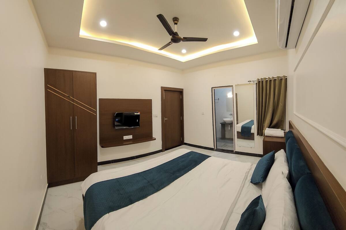 A hotel room with a bed, a TV mounted on the wall, a ceiling fan, and an air conditioning unit.