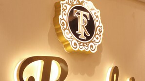 Eine Wand mit einem dekorativen Wappen und beleuchteter Schrift mit dem Schriftzug "Raahi".