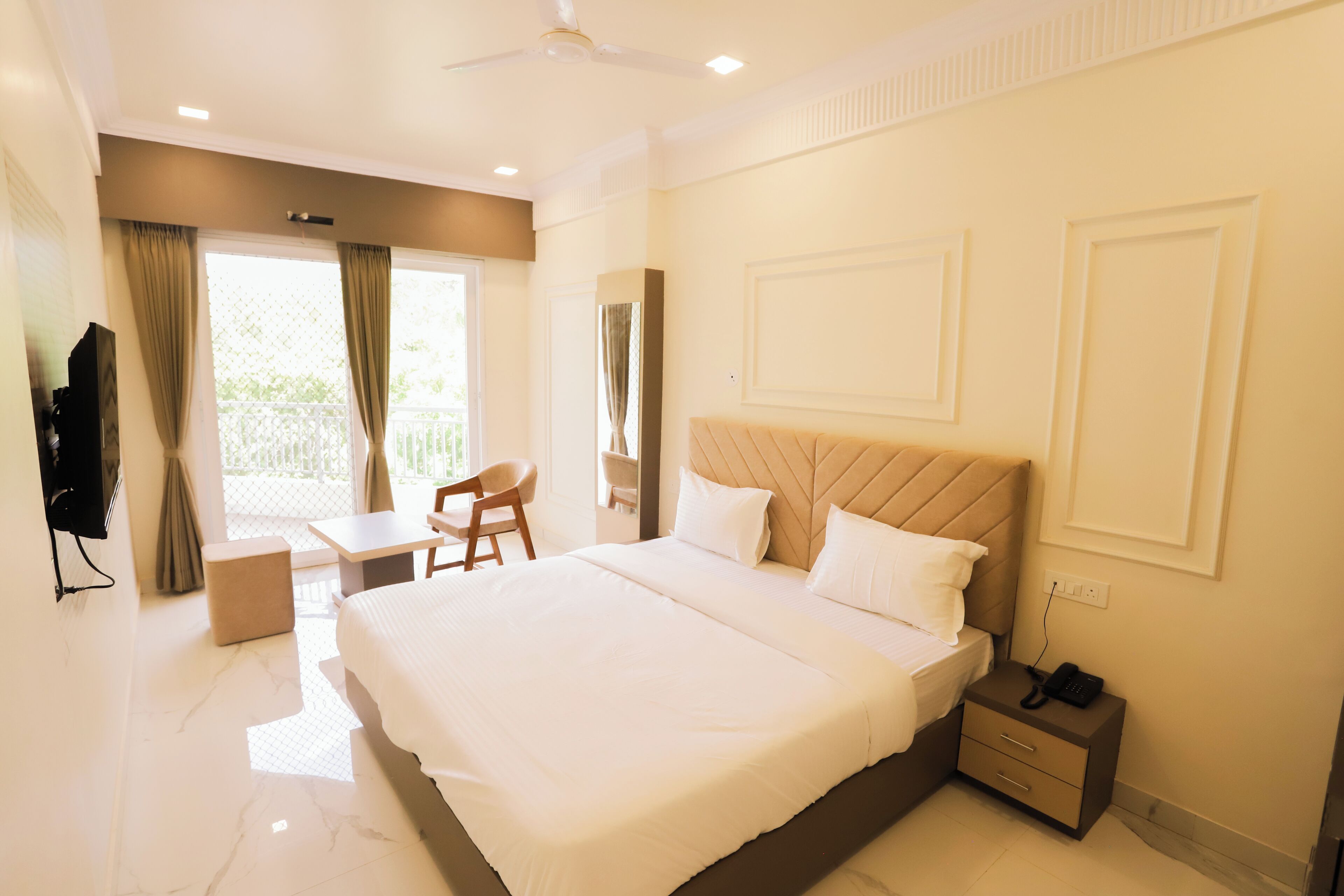 A hotel room with a large bed, a desk, a chair, a TV, and a balcony view.