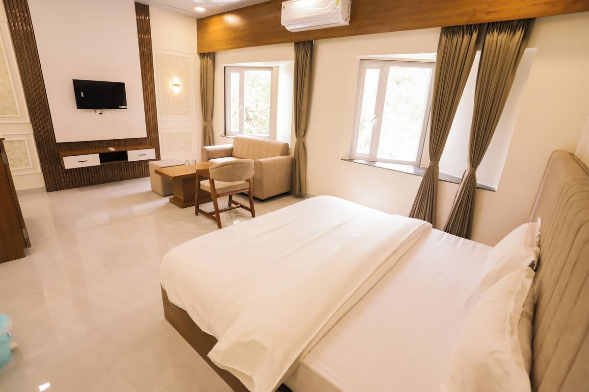 A hotel room with a large bed, a TV mounted on the wall, a desk, and a chair.