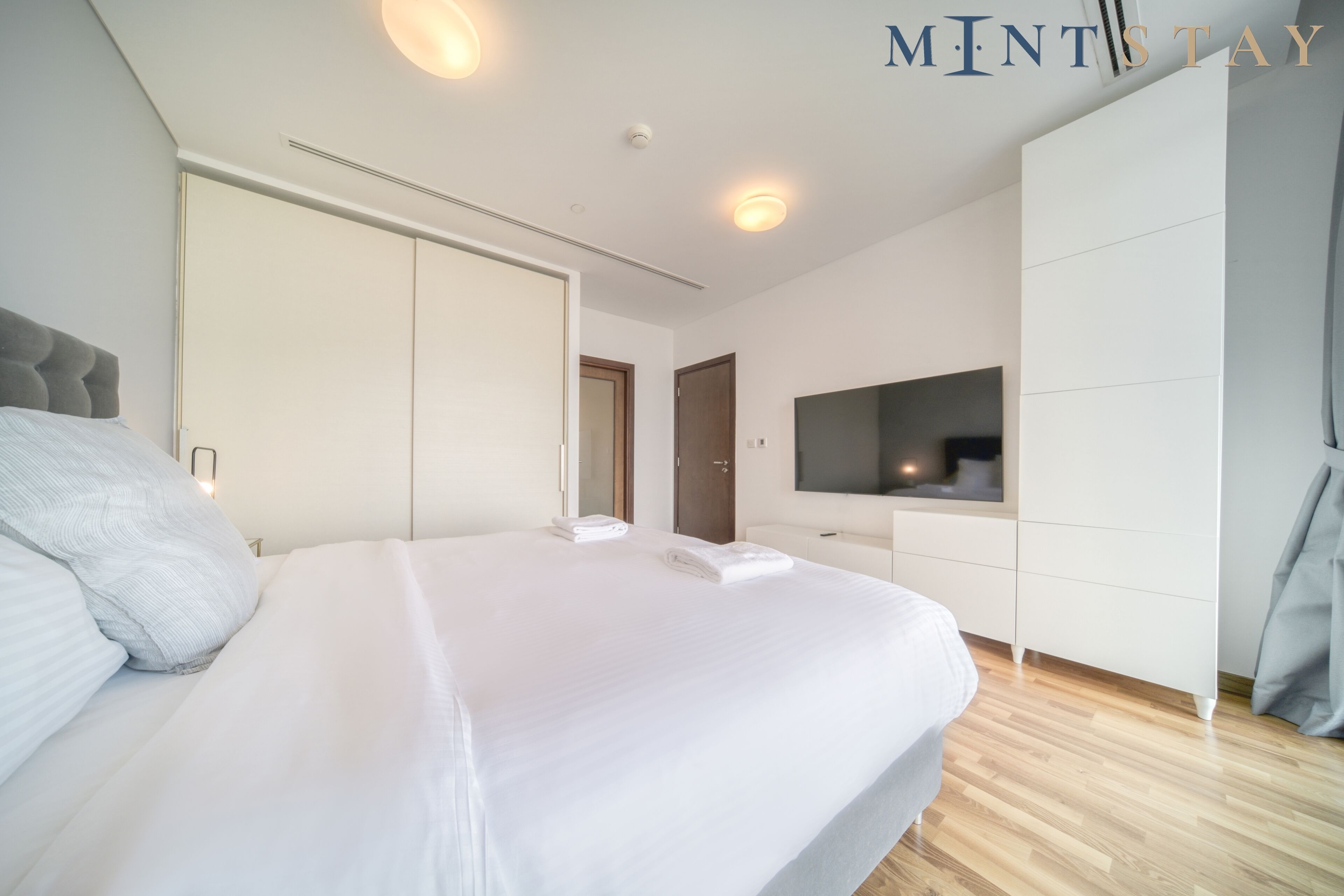 A modern bedroom with a large bed, a wardrobe, a TV, and a mirror.