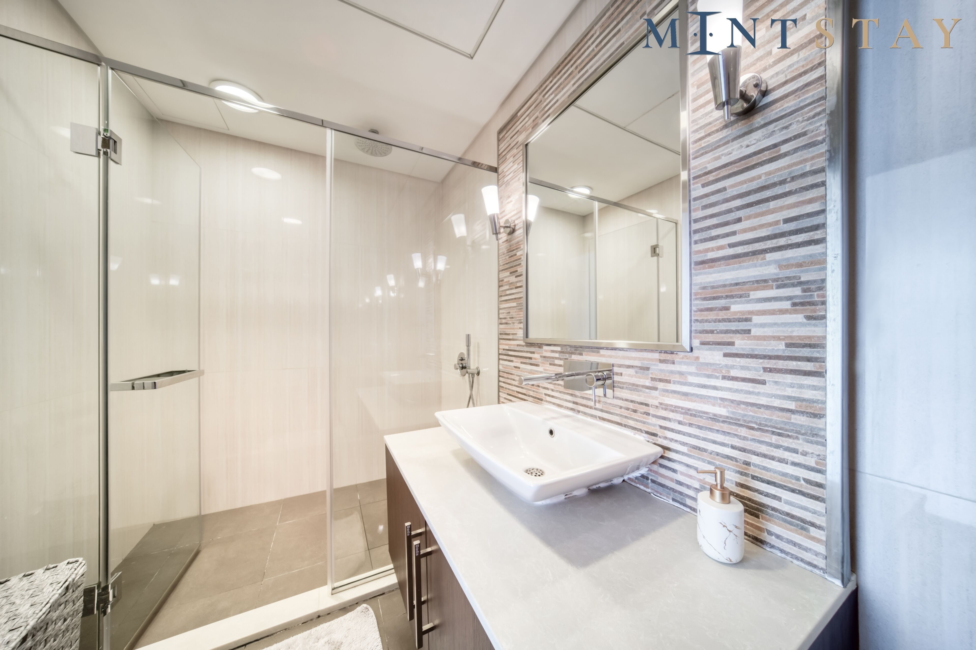 Un bagno moderno con box doccia in vetro, lavabo bianco e specchio con pannello di supporto strutturato.