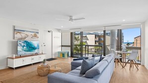 Ein modernes Wohnzimmer mit großem Fernseher, einer Couch, einem Couchtisch und einem Balkon mit Sitzgelegenheit.