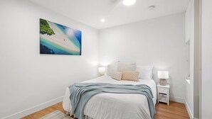 Ein Schlafzimmer mit einem Bett, einem Nachttisch, einer Lampe und einem Bild mit einer Strandansicht.