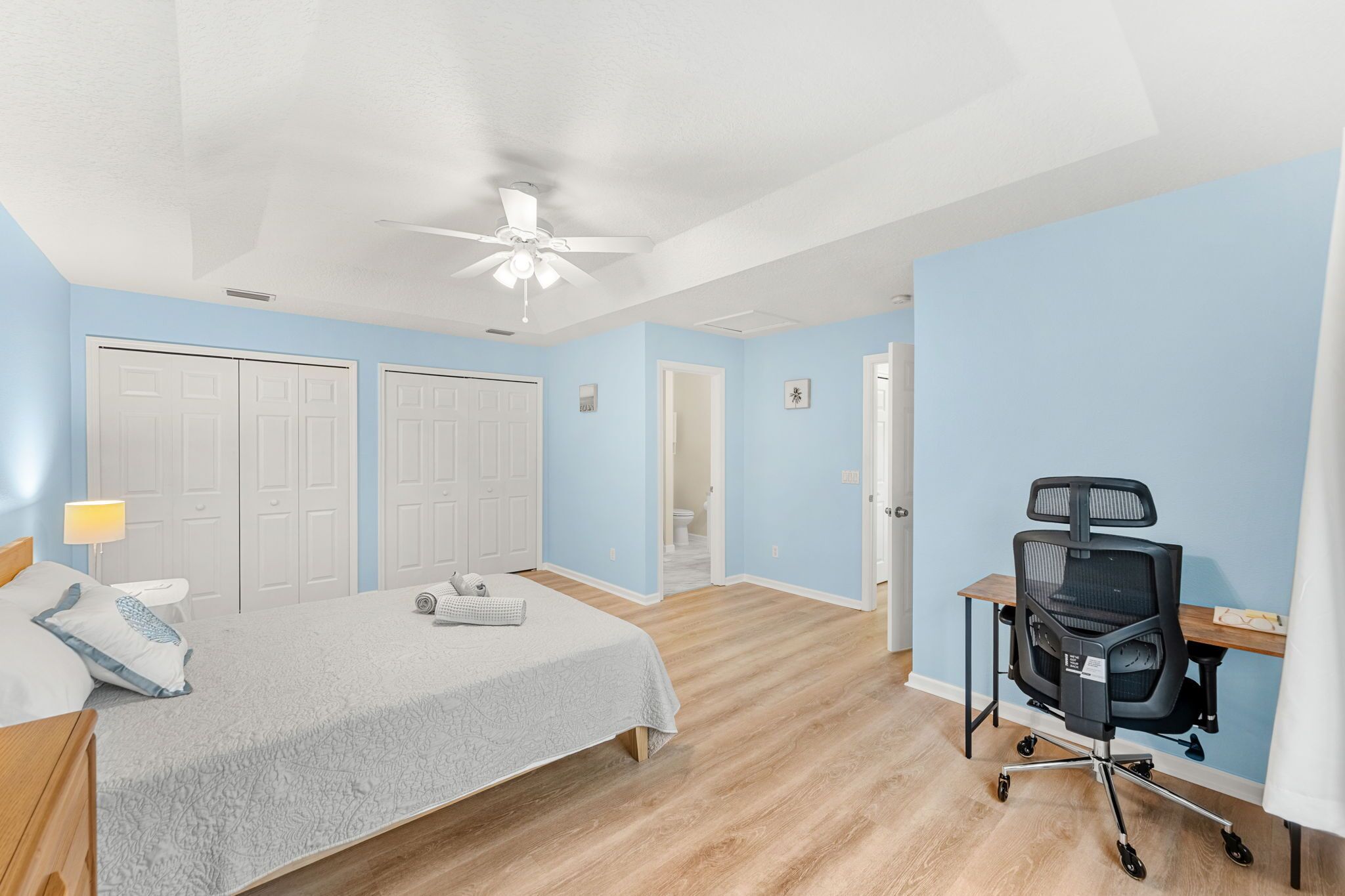 Une chambre à coucher avec un lit, un bureau, une chaise et un ventilateur de plafond.