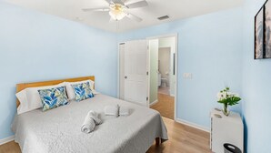 A bedroom with a bed, a ceiling fan, a door leading to a bathroom, and a small table with a vase. - 3-Bed with pool - Close to beach (Melbourne)