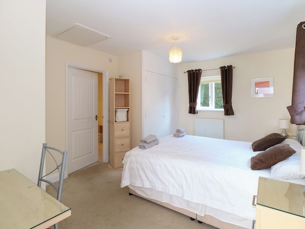 A bedroom with a bed, a desk, a wardrobe, and a window with curtains. - Rookyard Cottage (Halesworth)