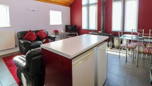 Una cocina moderna con lavavajillas integrado, un comedor con sillas a rayas y una sala de estar con sofá de cuero y cojines rojos.