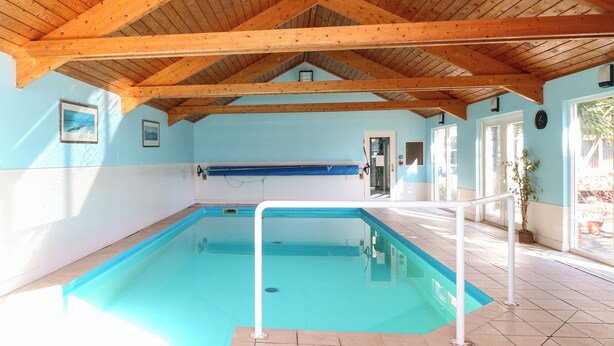 Una piscina interior con vigas de madera, agua azul y suelo de baldosas.
