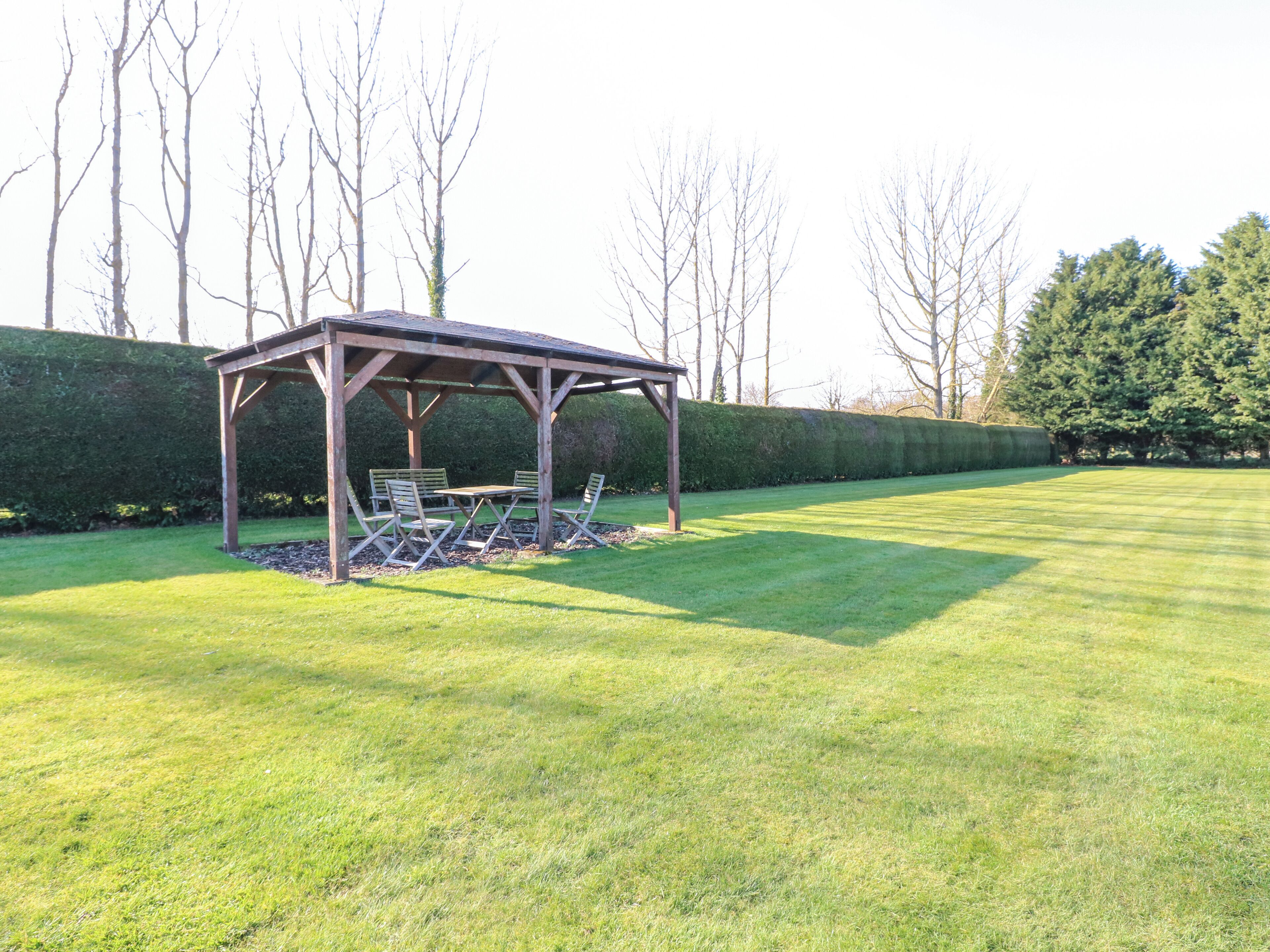 A wooden gazebo with a table and chairs in a well-maintained lawn area.