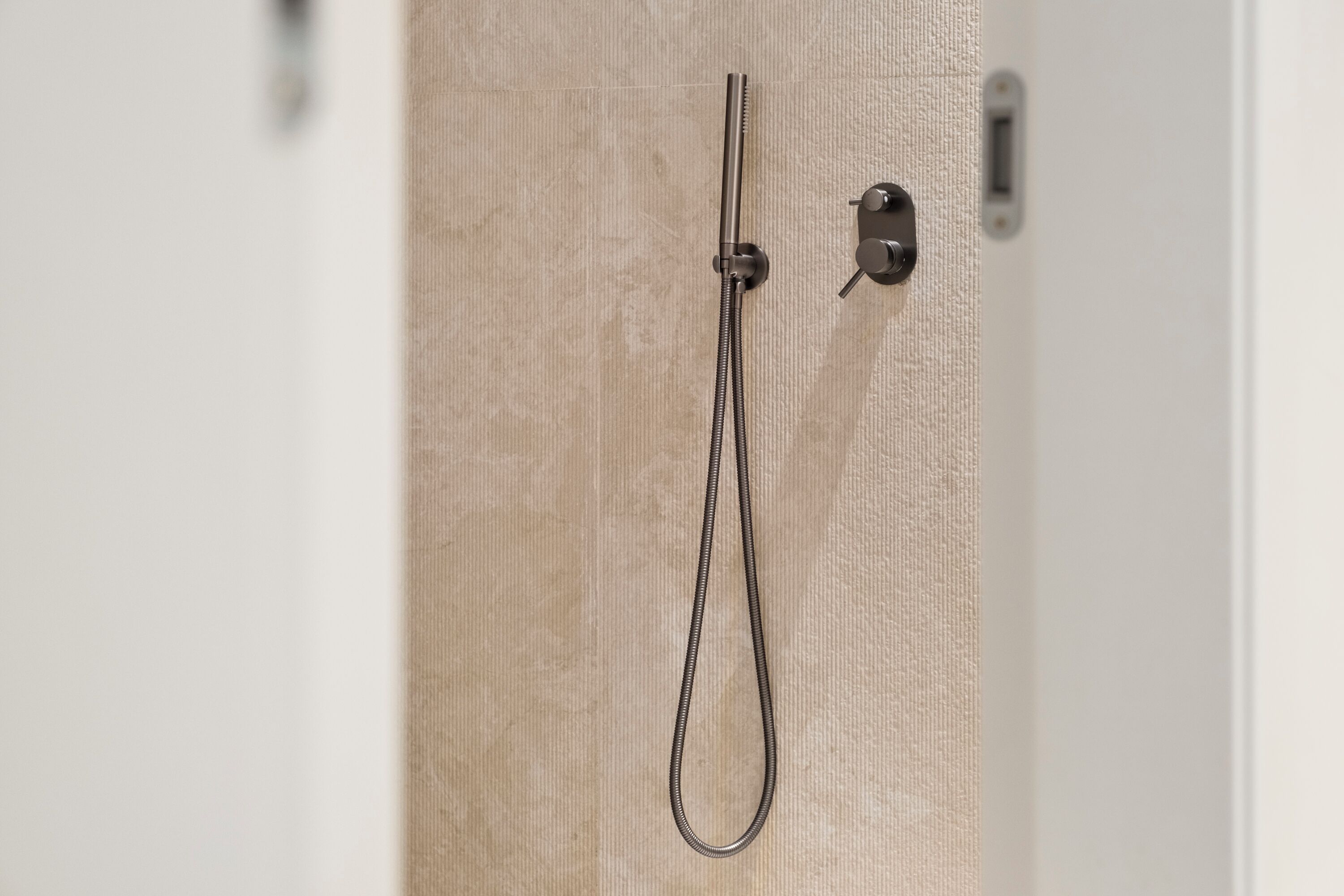 A shower with a handheld hose and a control panel on a beige wall.
