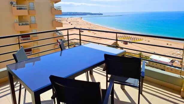 Ein Balkon mit Tisch und Stühlen mit Blick auf einen Strand und das Meer.