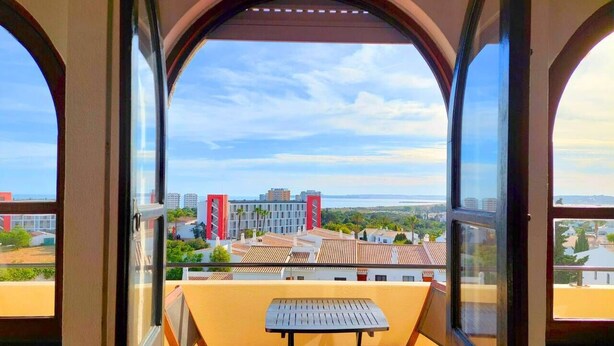 A balcony with a table and chairs, offering a view of buildings and a clear sky. - ALVOR - ALVOR HOLIDAYS II (Portimão)
