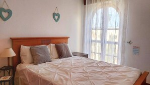 A neatly made bed with a wooden headboard, a bedside table with a lamp, and heart-shaped wall decorations. - ALVOR - ALVOR HOLIDAYS II (Portimão)