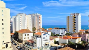 A coastal cityscape with high-rise buildings, a clear blue sky, and a view of the sea.