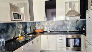 A modern kitchen with white cabinets, a black countertop, a microwave, an oven, and a sink.