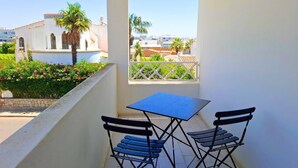 Un balcón con una mesa y dos sillas, con vista a un jardín de palmeras y edificios.
