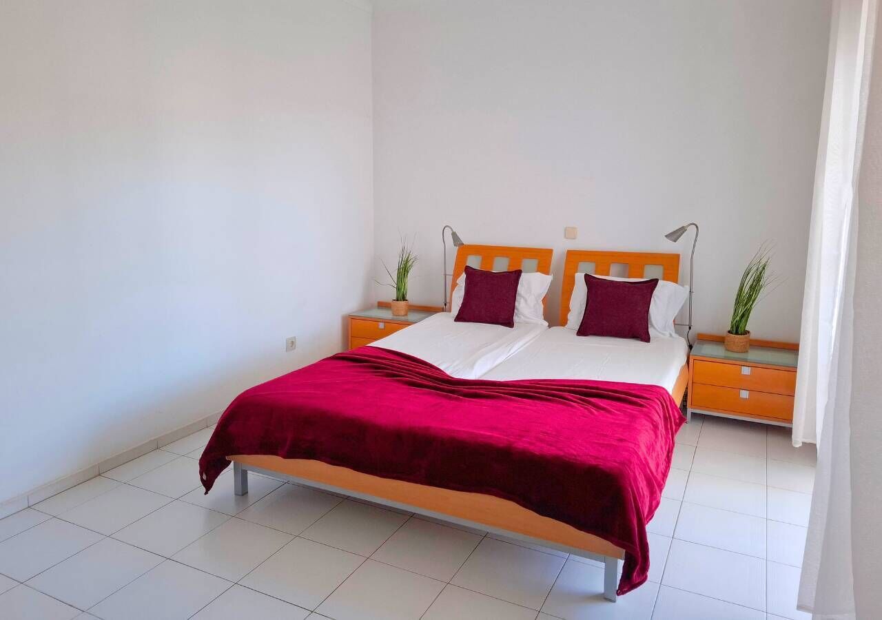 A bed with a red blanket, wooden headboard, and two bedside tables with lamps.