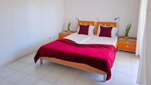 Una cama con un edredón rojo, cabecera de madera y dos mesitas de noche con lámparas.