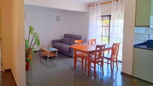 Un espacio habitable compacto con zona de comedor, un sofá, una mesita y una planta en maceta.