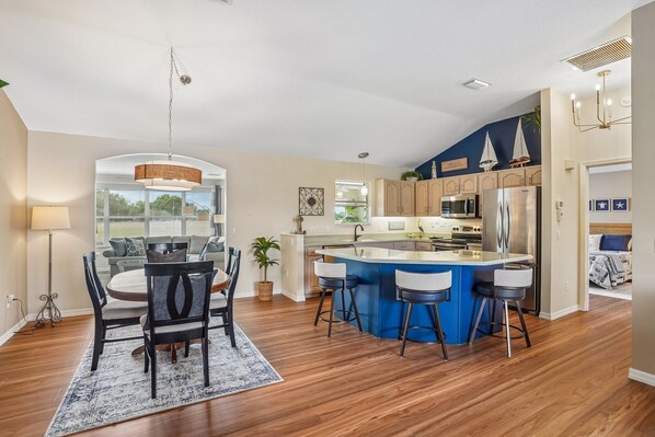 A modern kitchen with a central island, bar stools, and a dining area with a table and chairs.