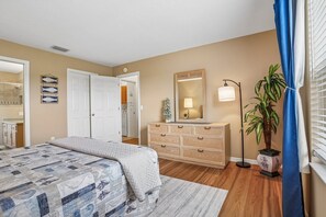 A bedroom with a bed, dresser, mirror, lamp, potted plant, and a door leading to another room. - Stunning sunsets, wildlife views & golf cart included for Villages lifestyle  (The Villages)