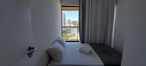 Ein modernes Hotelzimmer mit Bett, einem Fenster mit Vorhängen und Blick auf die Stadtlandschaft.
