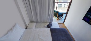 Ein kleines, modernes Zimmer mit einem Bett, einem Sessel und einem Fenster.