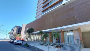 A modern building with a curved facade, a staircase leading to the entrance, and a parking area with cars.