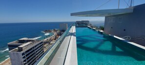 A pool with a view of the ocean and a building in the background. - COBAR0124 - Edifício Nau (Salvador)