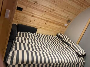 A bedroom with a wooden ceiling, a bed with a striped bedspread, and a black headboard. - Starview by Mirriemora l Shetland l St Ninians Isle l Cosy Pod (Bigton)