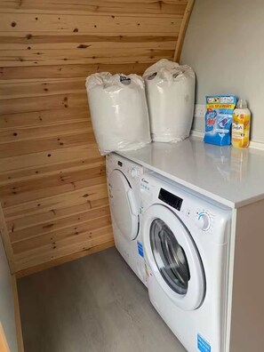 A compact laundry room with a front-loading washing machine, two large white bags on top, and detergent bottles on the counter.