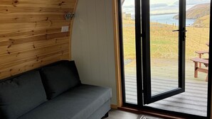 A cozy room with a grey sofa, wooden ceiling, and a large sliding glass door leading to an outdoor deck. - Starview by Mirriemora l Shetland l St Ninians Isle l Cosy Pod (Bigton)