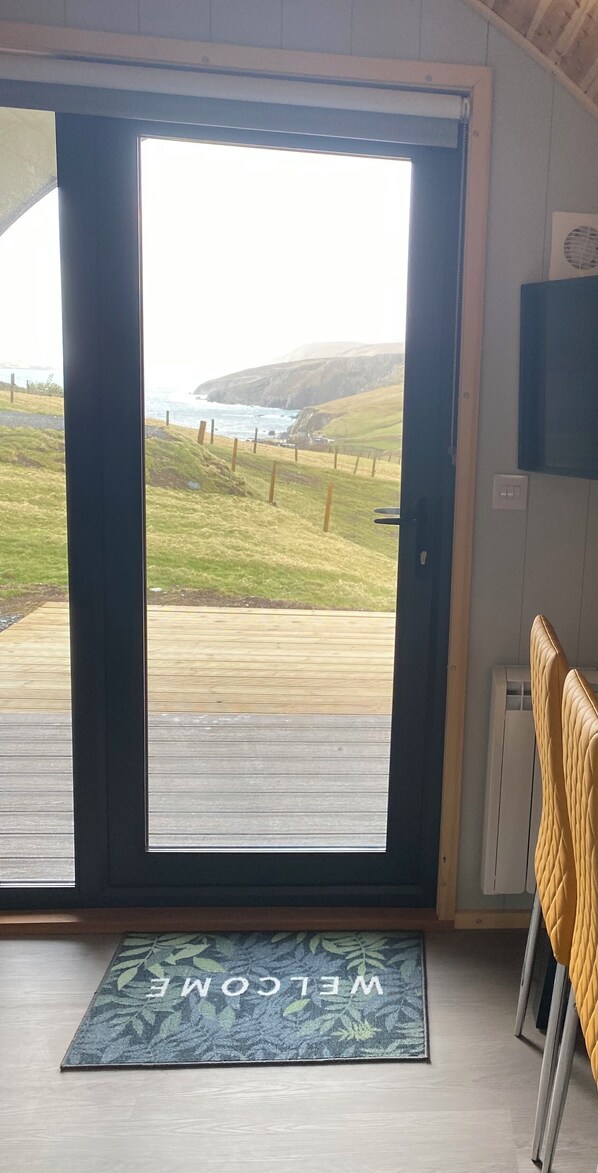 A door leading to a deck with a view of the ocean and hills.