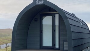 A modern, dark-colored pod-style accommodation with a wooden deck in front. - Starview by Mirriemora l Shetland l St Ninians Isle l Cosy Pod (Bigton)