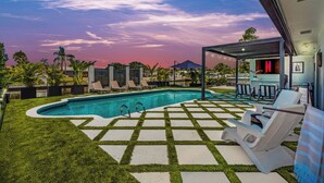 A swimming pool with a geometric tile pattern, surrounded by grass and palm trees.