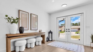 A modern interior with a wooden bench, white poufs, a white vase, and two framed artworks.