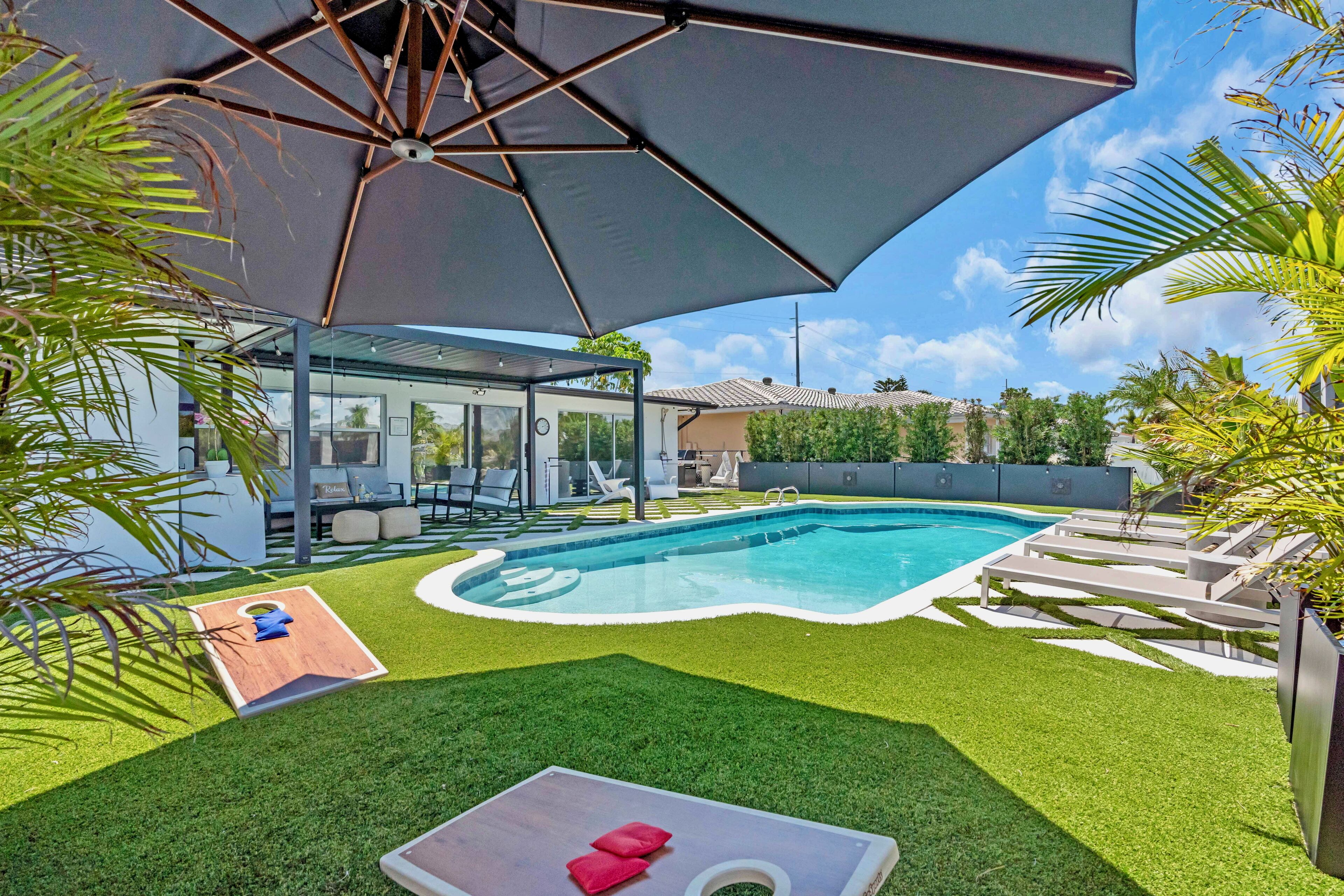 A backyard with a swimming pool, artificial grass, lounge chairs, and a glass-enclosed patio area.