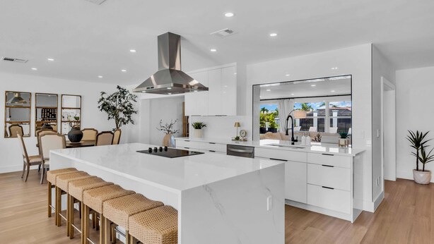 A modern kitchen with a large island, white cabinetry, and a stainless steel range hood.