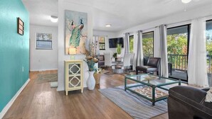 A spacious living room with a teal accent wall, a large painting, a glass coffee table, and a view of the outdoors. - Bradenton Breeze  (Bradenton)